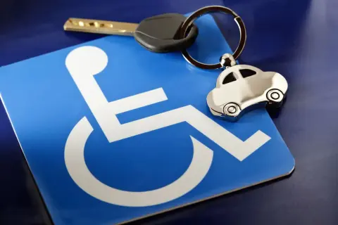 Chiave e portachiavi a forma di auto su un cartello blu con simbolo di disabilità. Possibile riferimento a invalidità civile 75 e bollo auto.