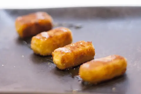 Friterad fetaost i stavar, gyllene och krispiga, serverade på en mörk tallrik med en lätt glasyr.