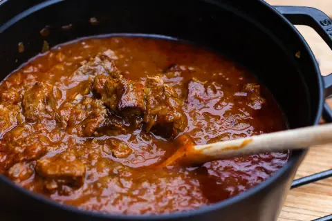 Ein dampfender Topf mit zartem Wiener Saftgulasch, das nach dem Originalrezept zubereitet wurde. Eine Holzschöpfkelle rührt in der köstlichen Sauce.