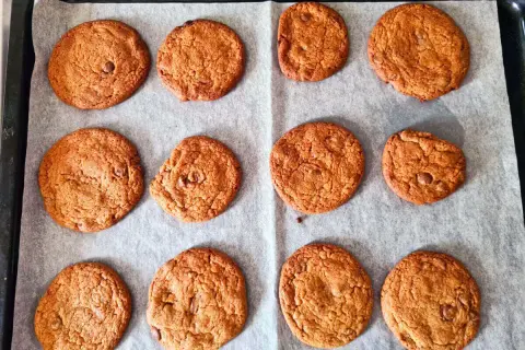 Nybakade chocolate chip cookies ligger på ett bakplåtspapper, redo att avnjutas.