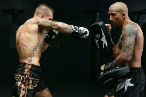 Two men practice boxing without sparring. One throws a punch while the other holds a pad to catch it.