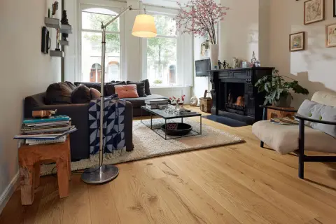 Gemütliches Wohnzimmer mit dunklem Sofa, Kamin und einem Sessel. Der used look des Holzboden und der Deko verleiht dem Raum Charakter.