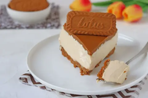 Una fetta di cheesecake Lotus, con biscotto e caramello, su un piatto bianco. Un morso su una forchetta.