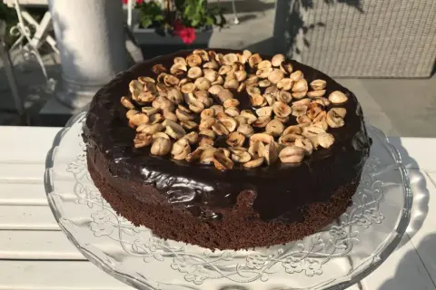 Czekoladowy tort z polewą i orzechami na szklanej paterze.