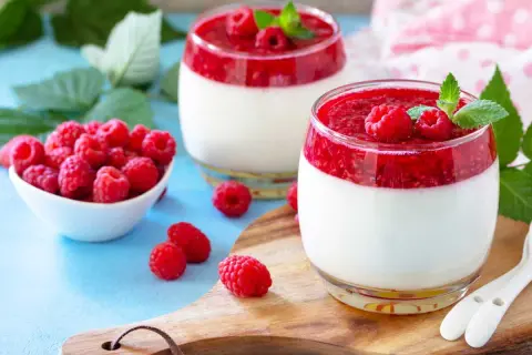 Deux panna cotta framboise, garnies de fruits rouges frais et de menthe, sur un plateau en bois.