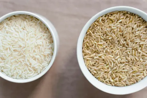 Zwei Schalen Reis: eine mit hellem Basmati oder Jasmin Reis, die andere mit braunem Reis.
