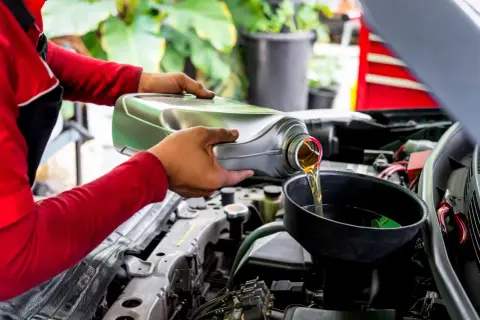 Mecánico vierte aceite nuevo en el motor de un coche, recordando que el aceite de coche caduca y debe cambiarse.