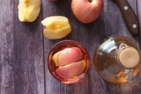 Ein Glas mit Apfelschnitzen und eine Flasche Apfelessig stehen bereit. Zeit, Apfelessig zu trinken!