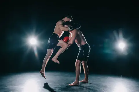 Two boxers spar intensely. One leaps, delivering a knee strike while the other defends. This dynamic action shows how boxers do calisthenics for explosive power.
