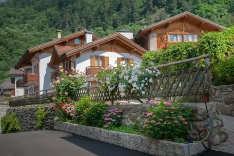 Case con balconi in legno e fiori colorati, incorniciate da un giardino rigoglioso. Un angolo di pace nel Val di Sole, dove si trova questo incantevole paesaggio.