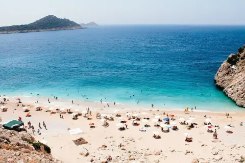Piękna pogoda w Antalyi! Słoneczny dzień na plaży z turkusową wodą, ludźmi kąpiącymi się i odpoczywającymi pod parasolami.