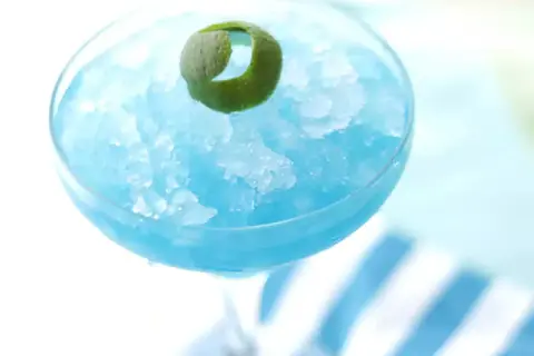 Orzeźwiający drink Błękitna Laguna, zmrożony i udekorowany skórką limonki, idealny na upalne dni.