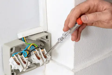 Ręka z próbnikiem napięcia sprawdza przewody w puszce elektrycznej. Dowiedz się, jak używać próbnik napięcia, by bezpiecznie pracować z instalacją.