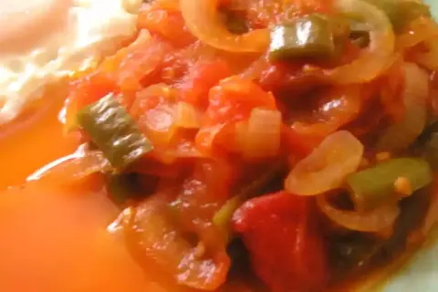 Une assiette de piperade recette, avec des poivrons verts, des oignons et des tomates mijotés, à côté d'un œuf au plat.