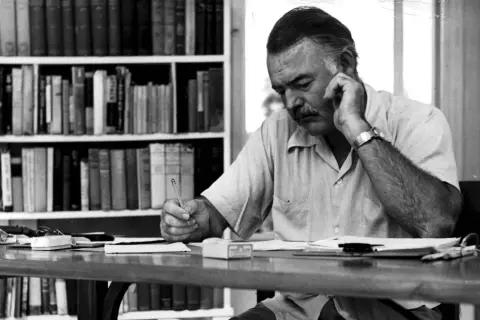 Ernest Hemingway pisze, myśląc o tym, komu bije dzwon. Streszczenie jego myśli widać w skupieniu na twarzy.