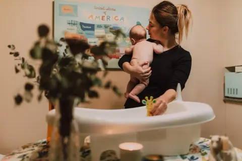 Mamma håller sitt barn redo för att bada. En leksak i form av en giraff ligger i badkaret.