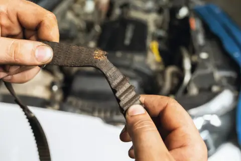 Zużyty pasek rozrządu, który wymaga wymiany, w rękach mechanika.