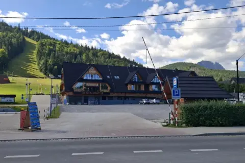 Parking pod Nosalem, z widokiem na górę i las. Restauracja z drewnianą elewacją, parking strzeżony.