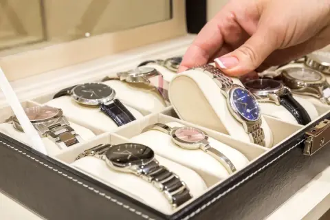 Una mano elige un reloj de una caja. Los relojes de pulsera, algunos de niquel que no se oxida, están ordenados en compartimentos.