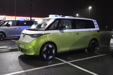 Zielony i srebrny VW ID. Buzz, jeden z niebieskimi światłami, parkuje nocą. Zasięg tych elektryków jest imponujący.