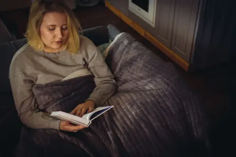 Kobieta z nadwrażliwością sensoryczną u dorosłych, otulona kocem, czyta książkę w przytulnym wnętrzu.