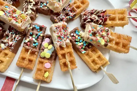 Bunte Waffeln am Stiel, getaucht in Schokolade und bestreut mit Streuseln und bunten Zuckerlinsen, laden zum Naschen ein.