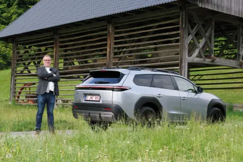Man i kavaj står bredvid silverfärgad Toyota bz4x under ett gammalt träskjul.