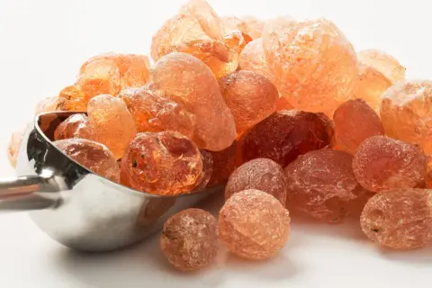 Grains ambrés de gomme arabique dans une cuillère métallique. Qu'est-ce que la gomme arabique ? Une résine naturelle aux multiples usages.
