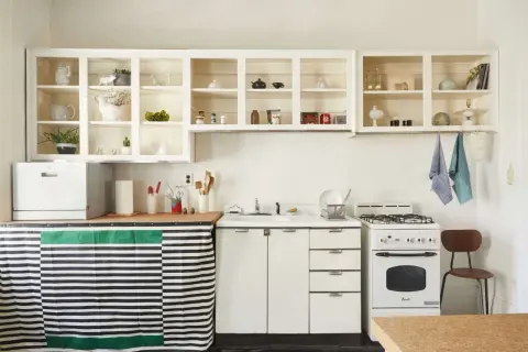 A cozy kitchen with open shelving displaying decorative items. A striped curtain hides the dishwasher, showcasing clever rental friendly upgrades.