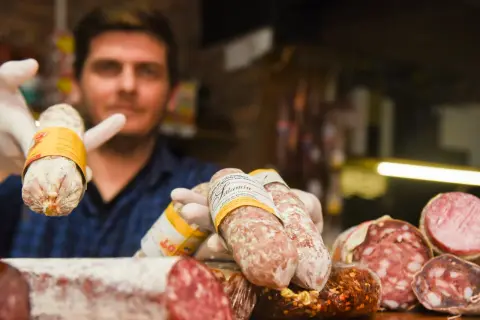 Un hombre con guantes blancos muestra varios tipos de salami, un embutido curado.