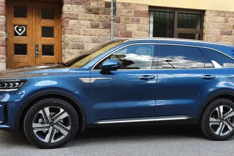 Blå laddhybrid diesel Kia Sorento parkerad framför en tegelbyggnad med en trädörr med ett hjärta.