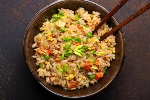 Un piatto fumante di riso alla cantonese ricetta originale, con piselli, carote, uova e cipollotto fresco, pronto per essere gustato con le bacchette.