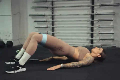 Kobieta wykonuje ćwiczenie glute bridge z taśmą oporową na udach.
