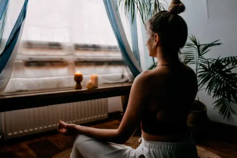Mujer meditando en un espacio para meditar en casa, con velas encendidas y plantas.