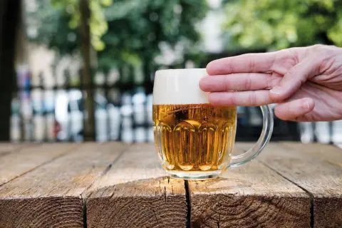 Dłoń dotyka gęstej piany na kuflu piwa, pokazując, jak powstaje piana.