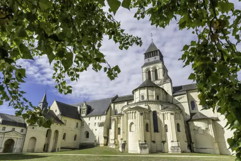 L'abbaye de Fontevraud, vue à travers des feuilles vertes. Combien de temps pour visiter Fontevraud ? Prévoyez une journée entière pour explorer ce site historique.