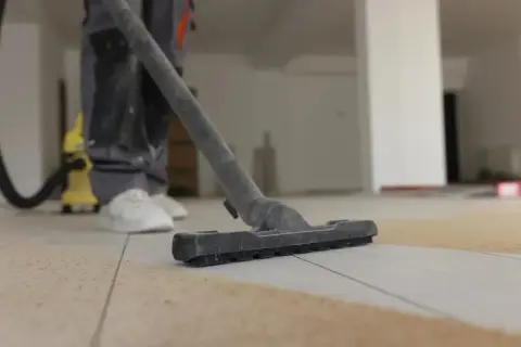 Un ouvrier utilise un aspirateur pour nettoyer le carrelage après le jointoiement. La poussière et les débris sont aspirés.
