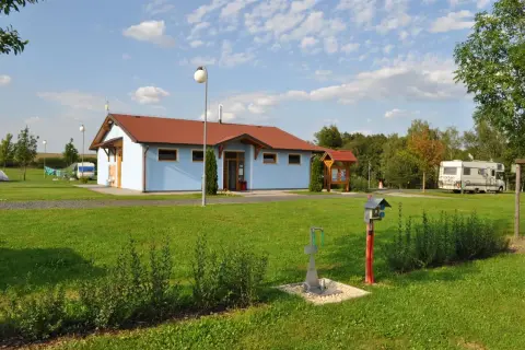 Ein hellblaues Gebäude mit rotem Dach auf dem Camping Vaclav. Wohnmobile und Zelte sind auf dem Rasen zu sehen.
