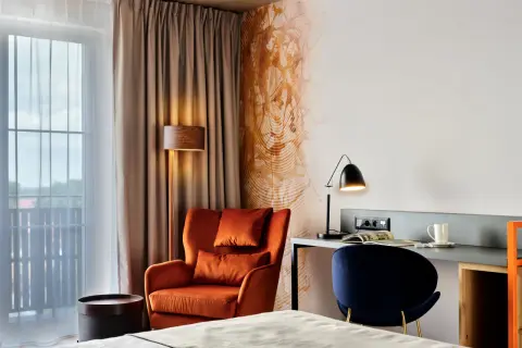 Przytulny pokój w **Bergo Hotel Szklarska Poręba**: pomarańczowy fotel, biurko z lampką i granatowe krzesło.