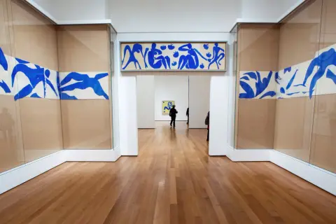 Gallery hallway showcasing Henri Matisse obras: blue cut-outs of figures adorn the walls, with a long horizontal piece above an archway and flowing designs on either side.