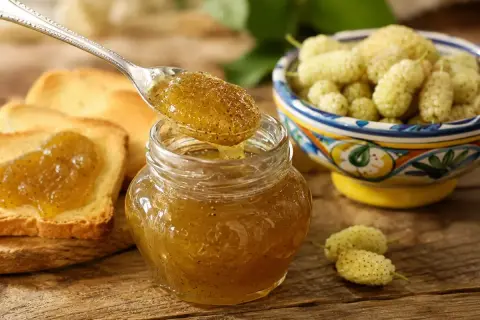 Marmellata di gelsi bianchi su pane tostato, con una ciotola di frutti freschi e un cucchiaino che ne raccoglie una porzione.