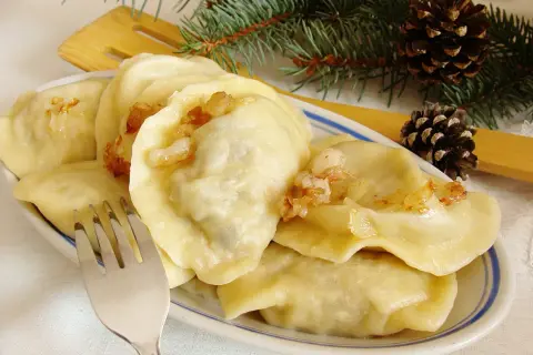 Pyszne pierogi z mięsem i kapustą, okraszone skwarkami, na talerzu z gałązką sosny i szyszkami.