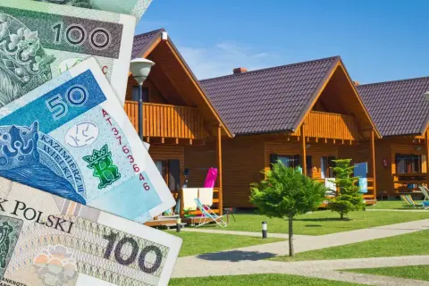 Polskie banknoty na tle drewnianych domków letniskowych.