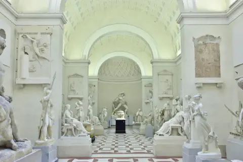 Interno della Galleria dell'Accademia con sculture classiche in marmo bianco, pavimentazione a scacchi e soffitto a volta.