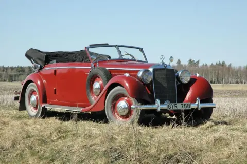 Röd cabriolet, en av de äldre tyska bilarna, parkerad på en äng med skog i bakgrunden.