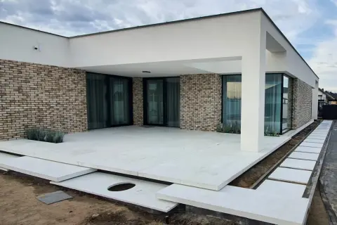 Nowoczesny dom z ceglaną elewacją i tarasem z jasnego, **betonu szczotkowanego**.