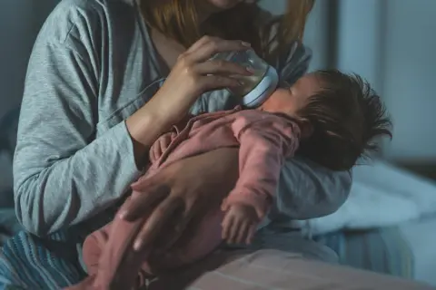 Mama karmi butelką noworodka, dbając o jego potrzeby. Mały brzuszek mieści niewielką ilość mleka, co odzwierciedla pojemność żołądka noworodka.