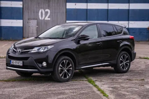 Czarny, używany Toyota RAV4 z salonu, zaparkowany przed budynkiem z numerem 02.