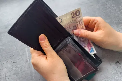 Ręce wkładają banknot 20 zł do portfela. Zastanawiasz się, po jakim czasie od zarejestrowania wypłacany jest zasiłek dla bezrobotnych?