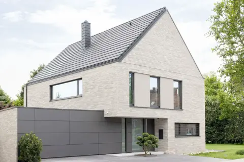 Modernes Haus mit hellem Klinker, das nicht gestrichen ist. Graues Dach, Garage und Fensterrahmen.
